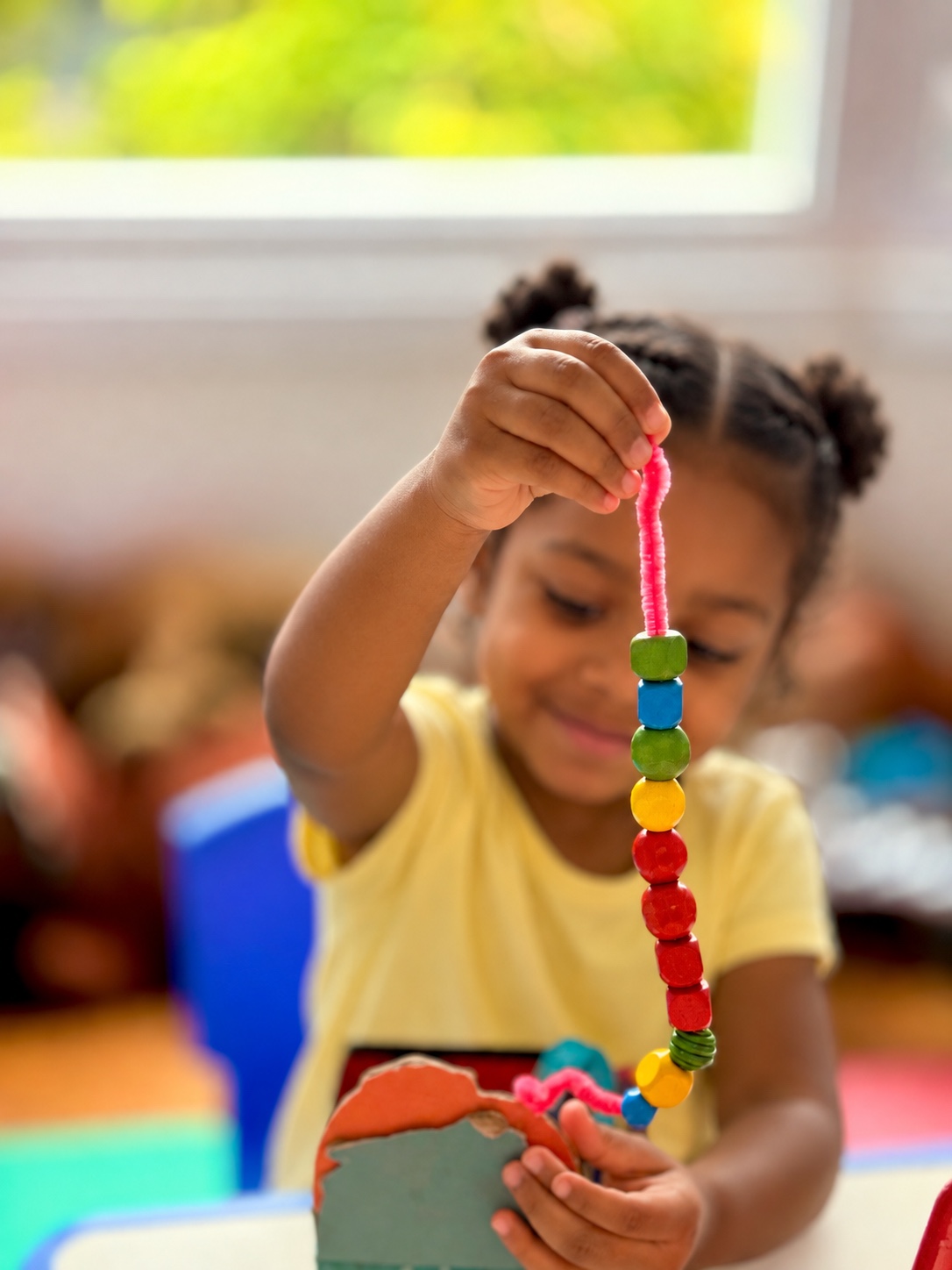 A little learner proudly showing colourful bead threading at Little Stars Kidz